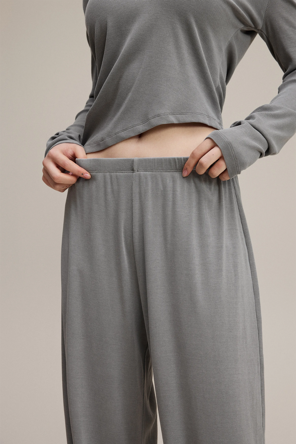 Person wearing gray long-sleeve top and wide-leg pants on a beige background