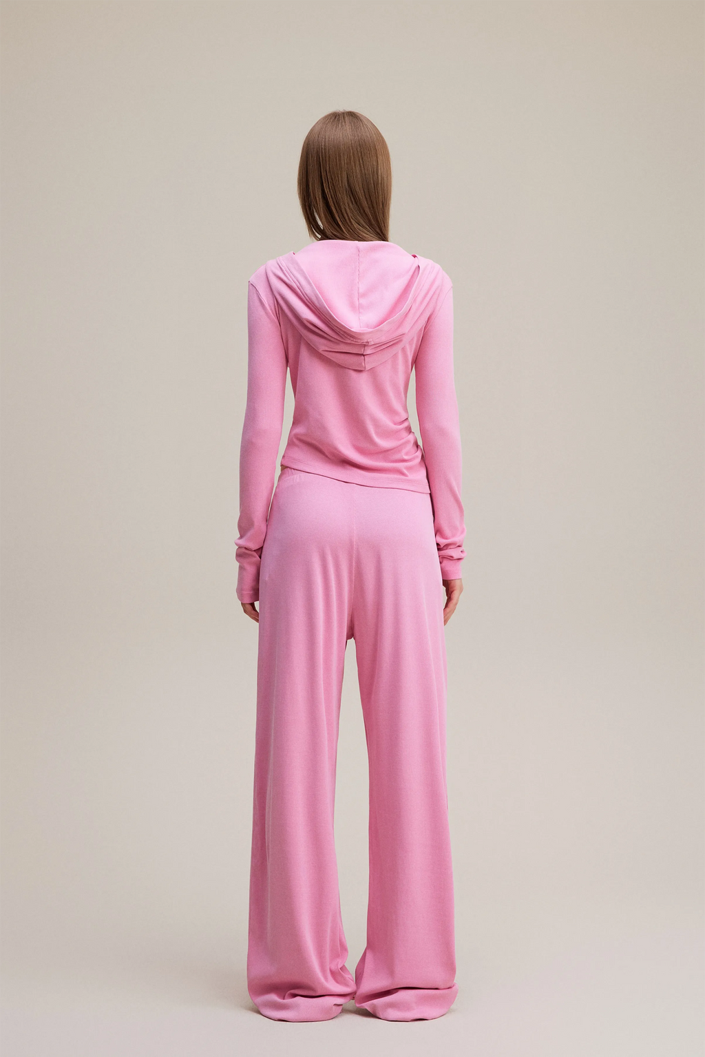 Person wearing a pink hoodie and pants set on a beige background