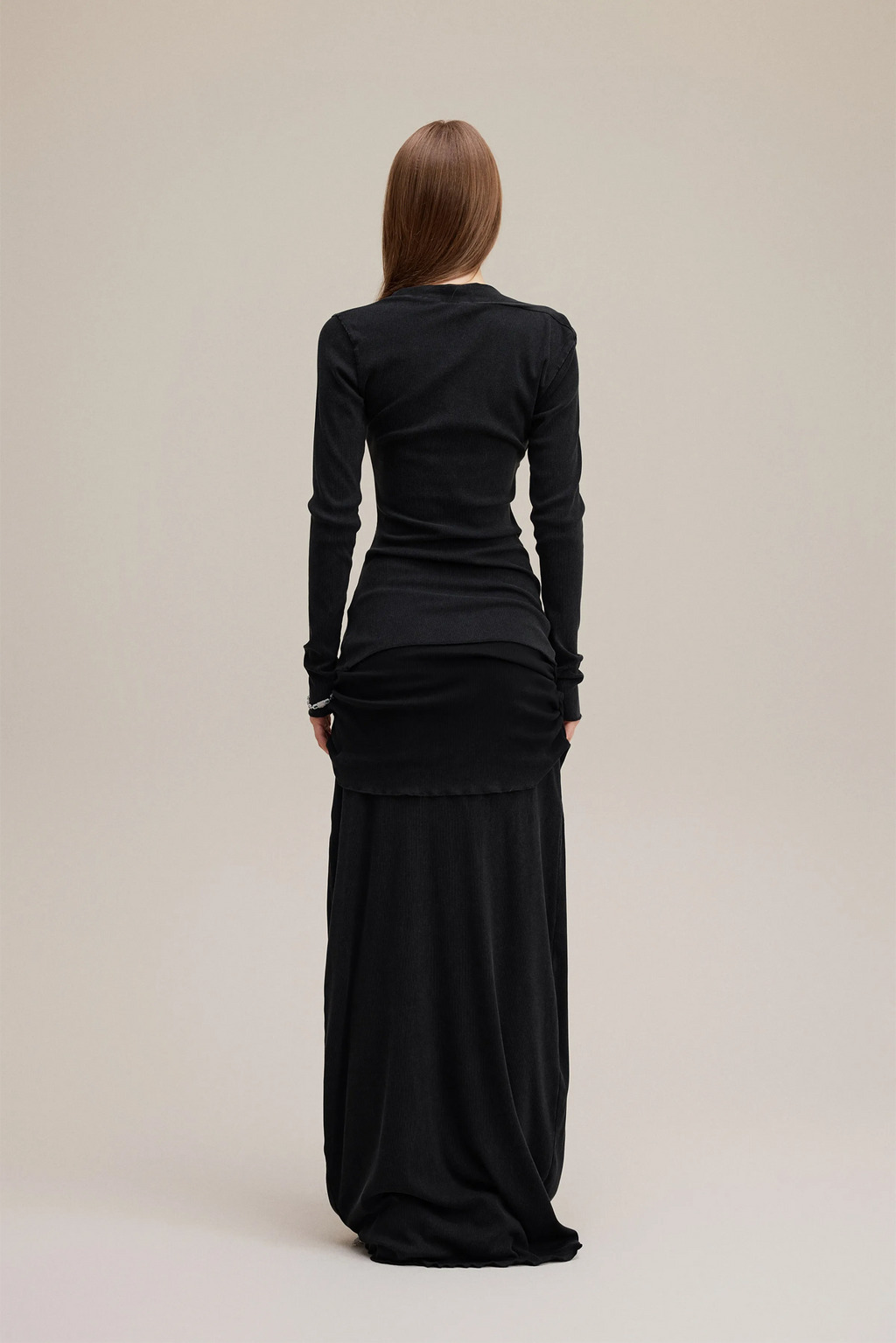 Woman wearing a black long-sleeve top and black skirt on a beige background