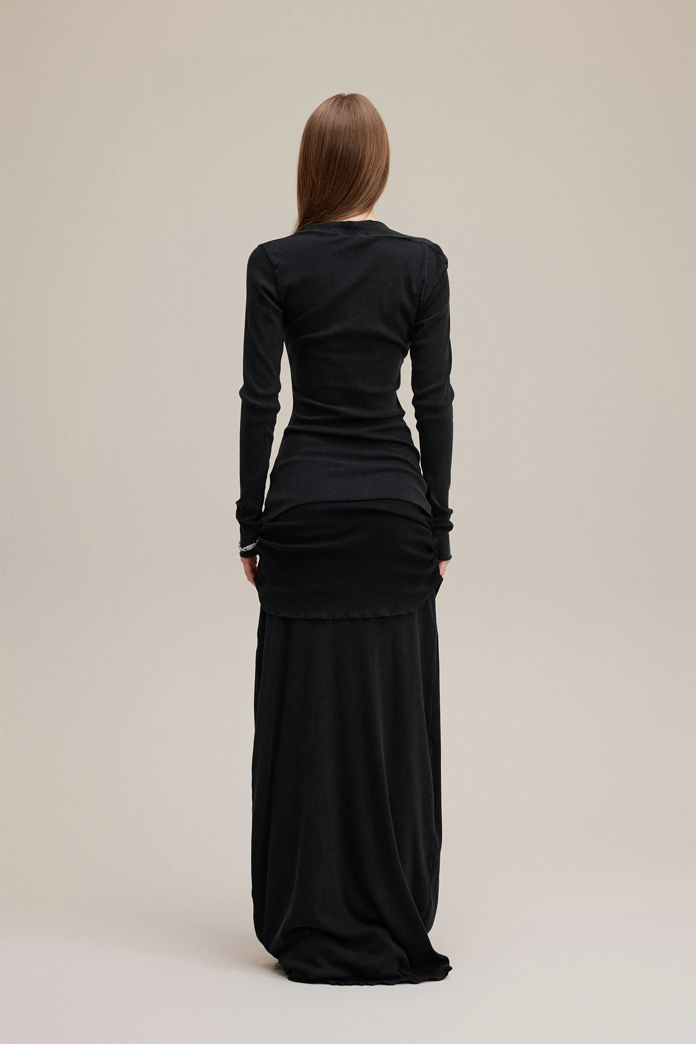 Woman wearing a black long-sleeve top and black skirt on a beige background