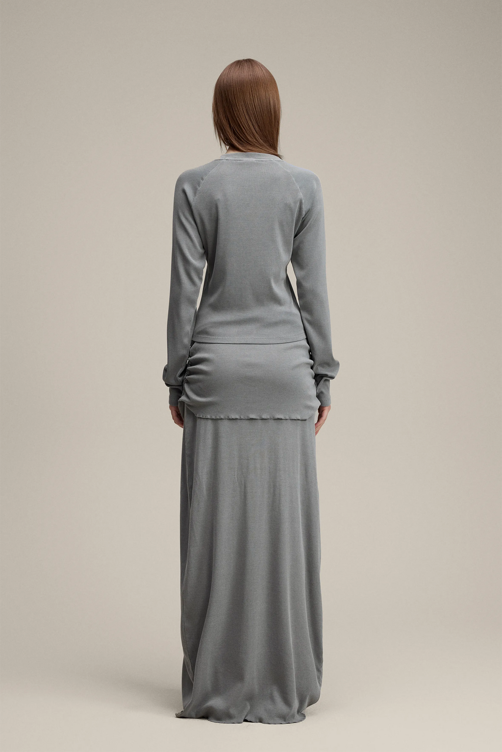 Woman wearing a gray long-sleeve top and long skirt set on a beige background