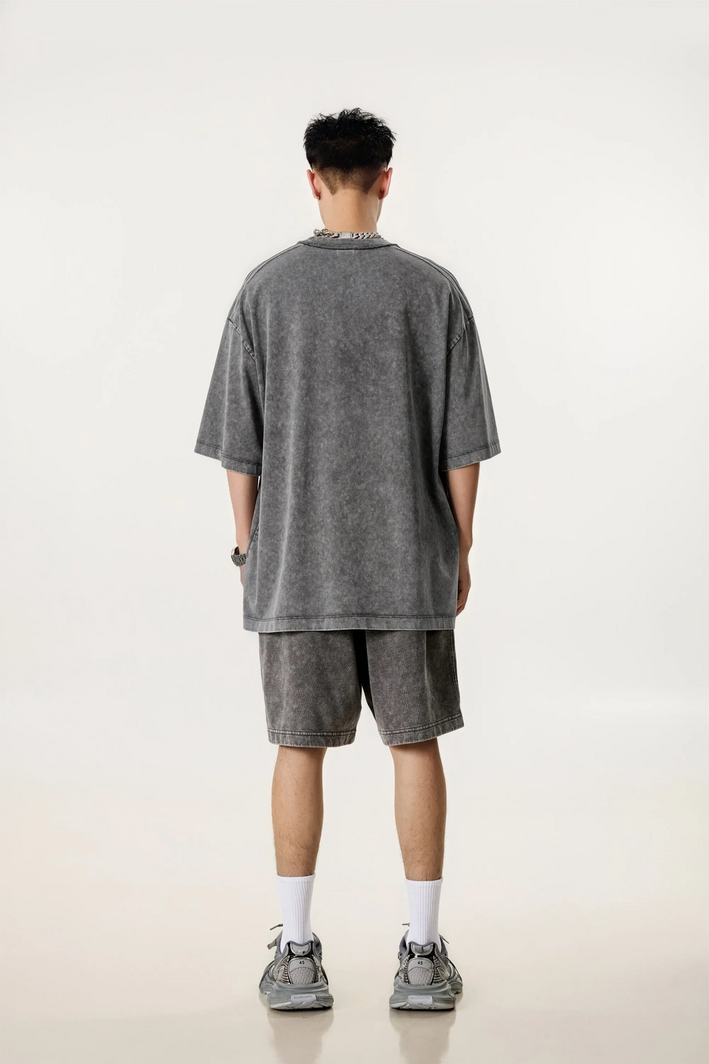Person wearing a gray oversized t-shirt and shorts set on a white background