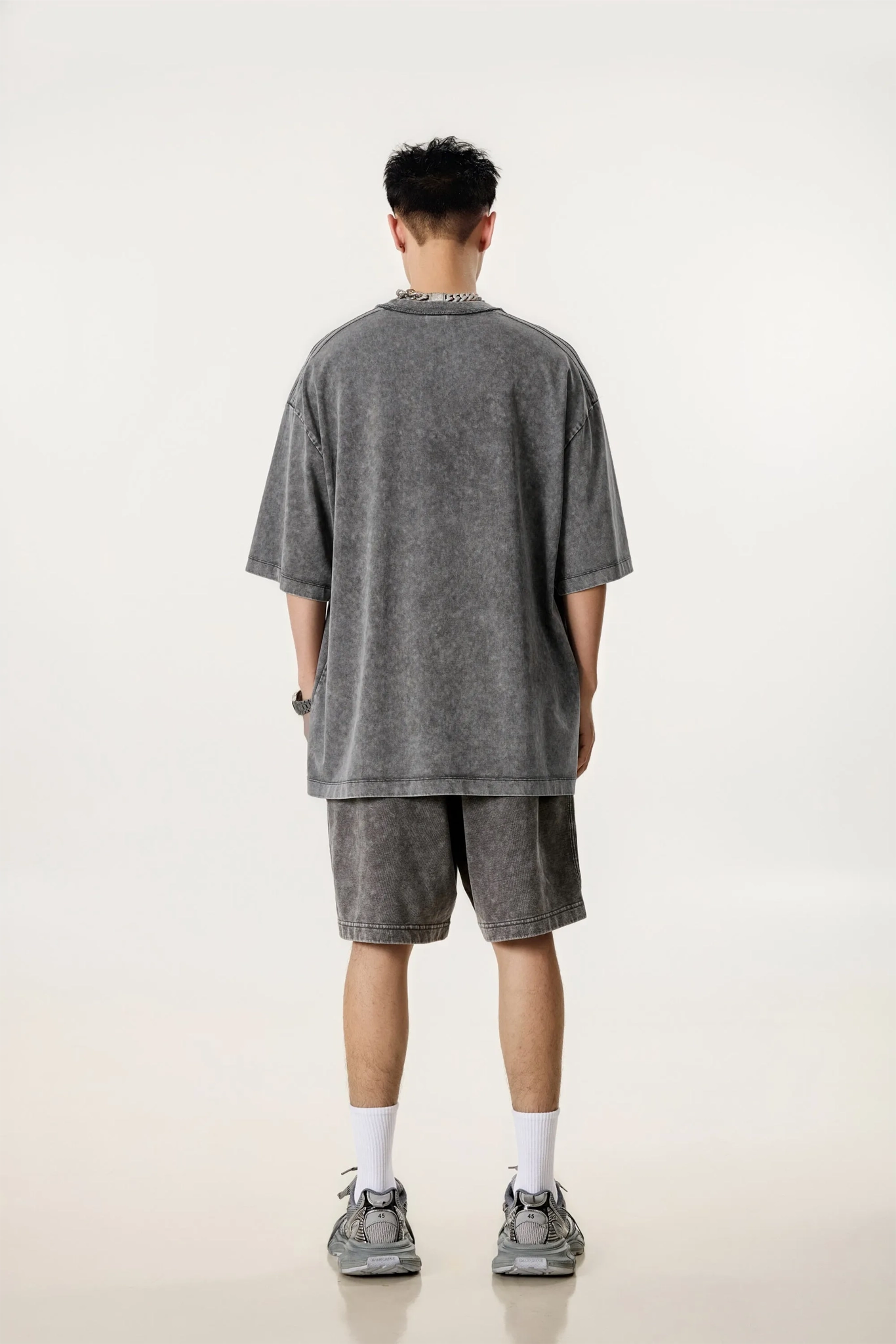 Person wearing a gray oversized t-shirt and shorts set on a white background