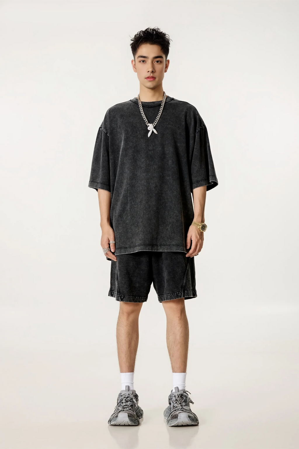 Person wearing a dark oversized t-shirt and shorts with sneakers on a white background