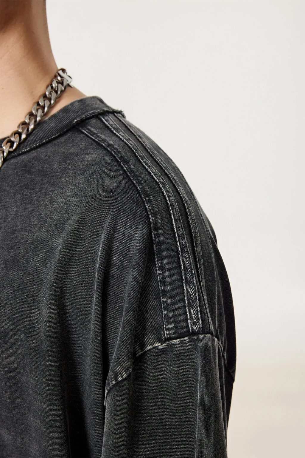 Close-up of a person wearing a dark gray distressed denim jacket with a blurred background