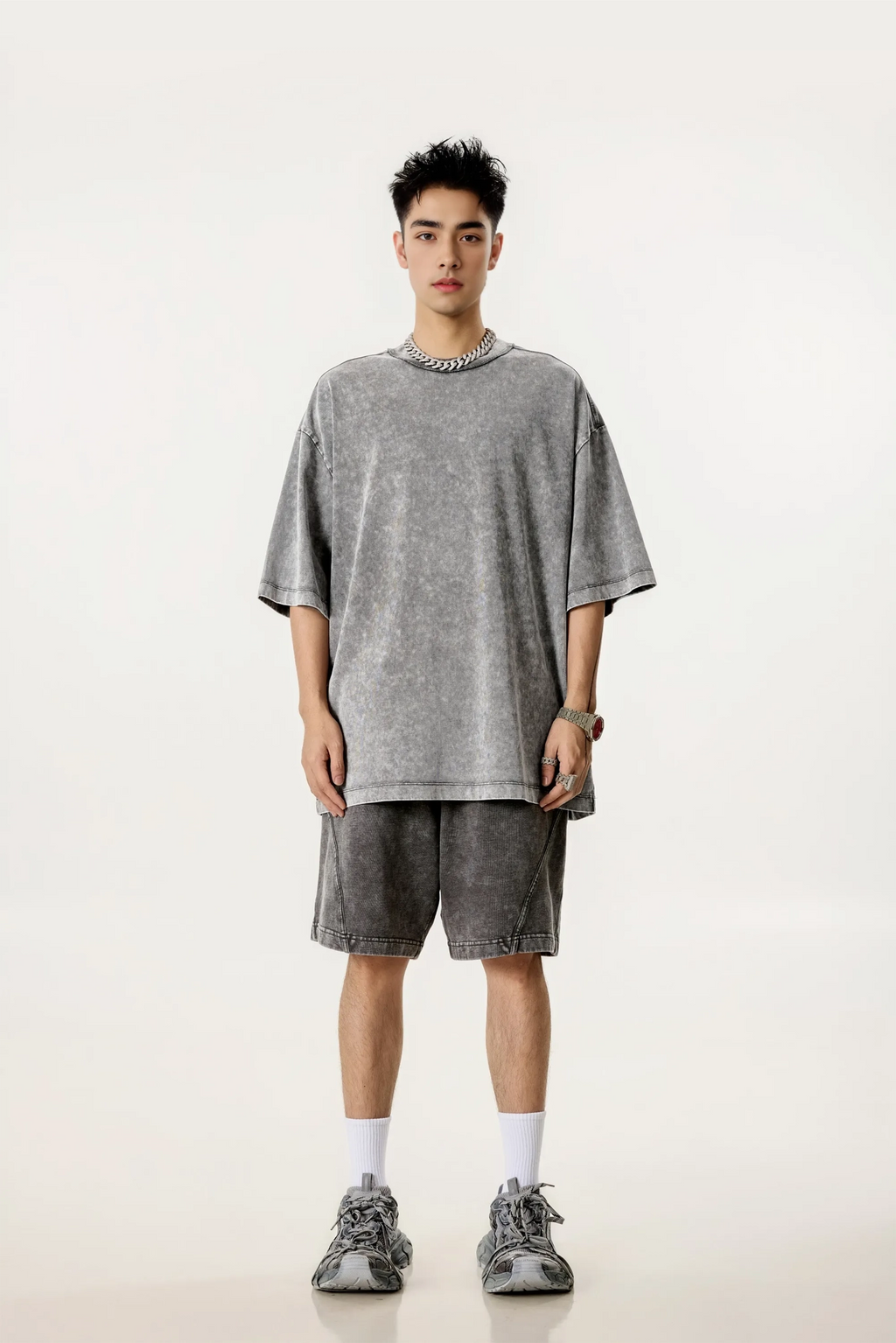 Person wearing a gray oversized t-shirt and shorts set on a white background