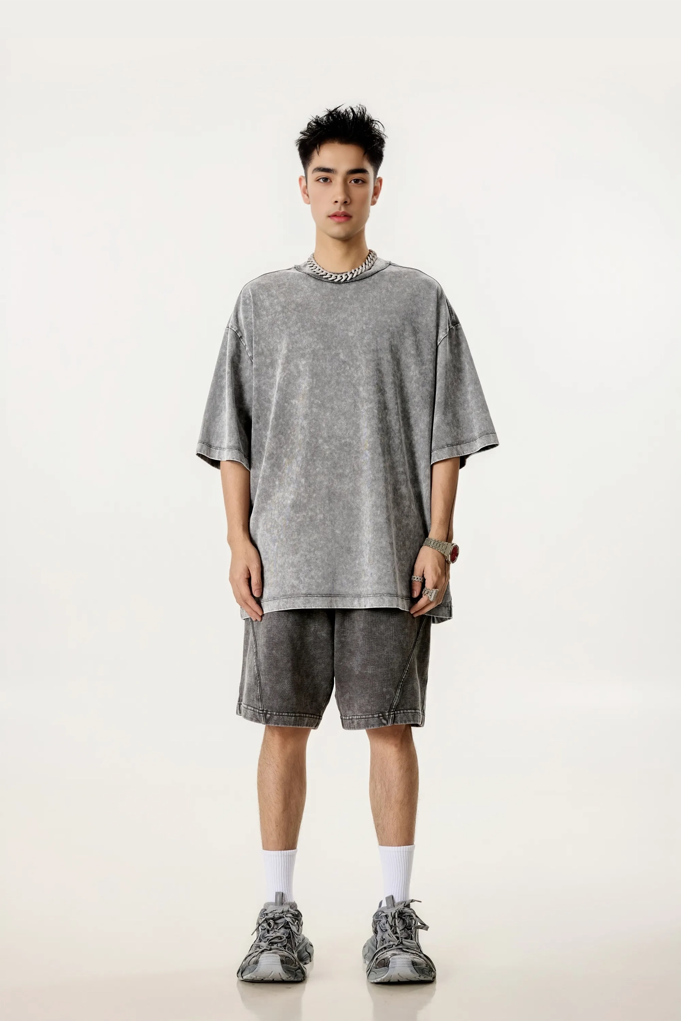 Person wearing a gray oversized t-shirt and shorts set on a white background