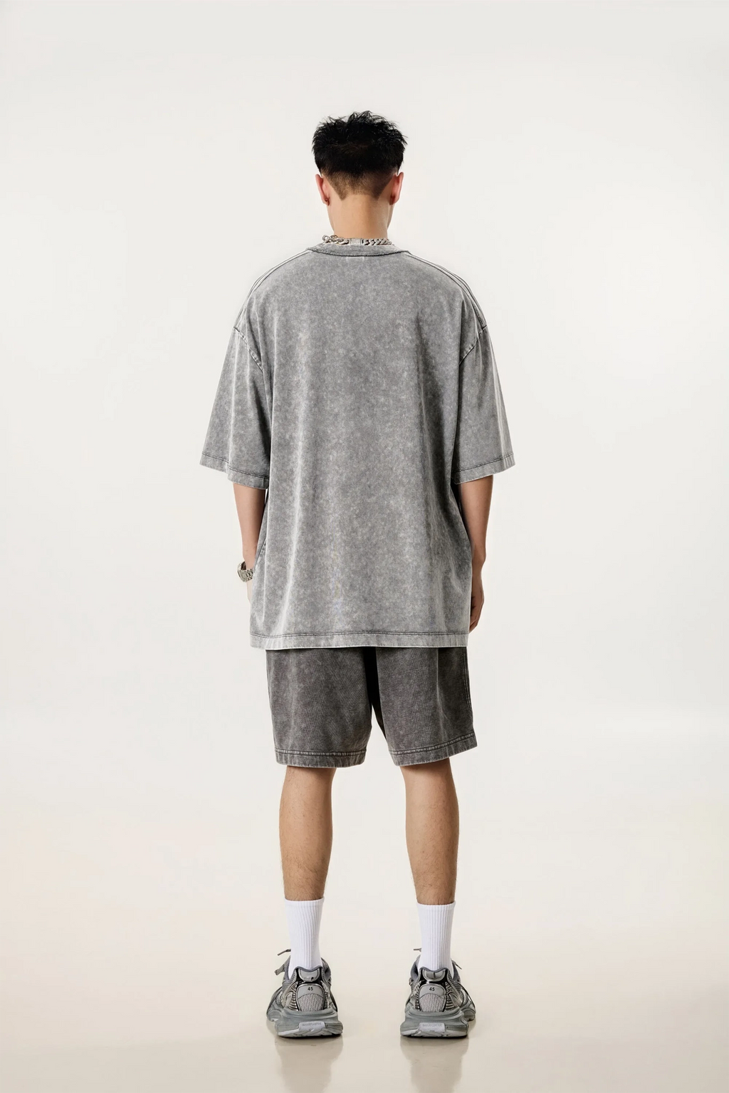 Person wearing a gray oversized t-shirt and shorts set on a white background