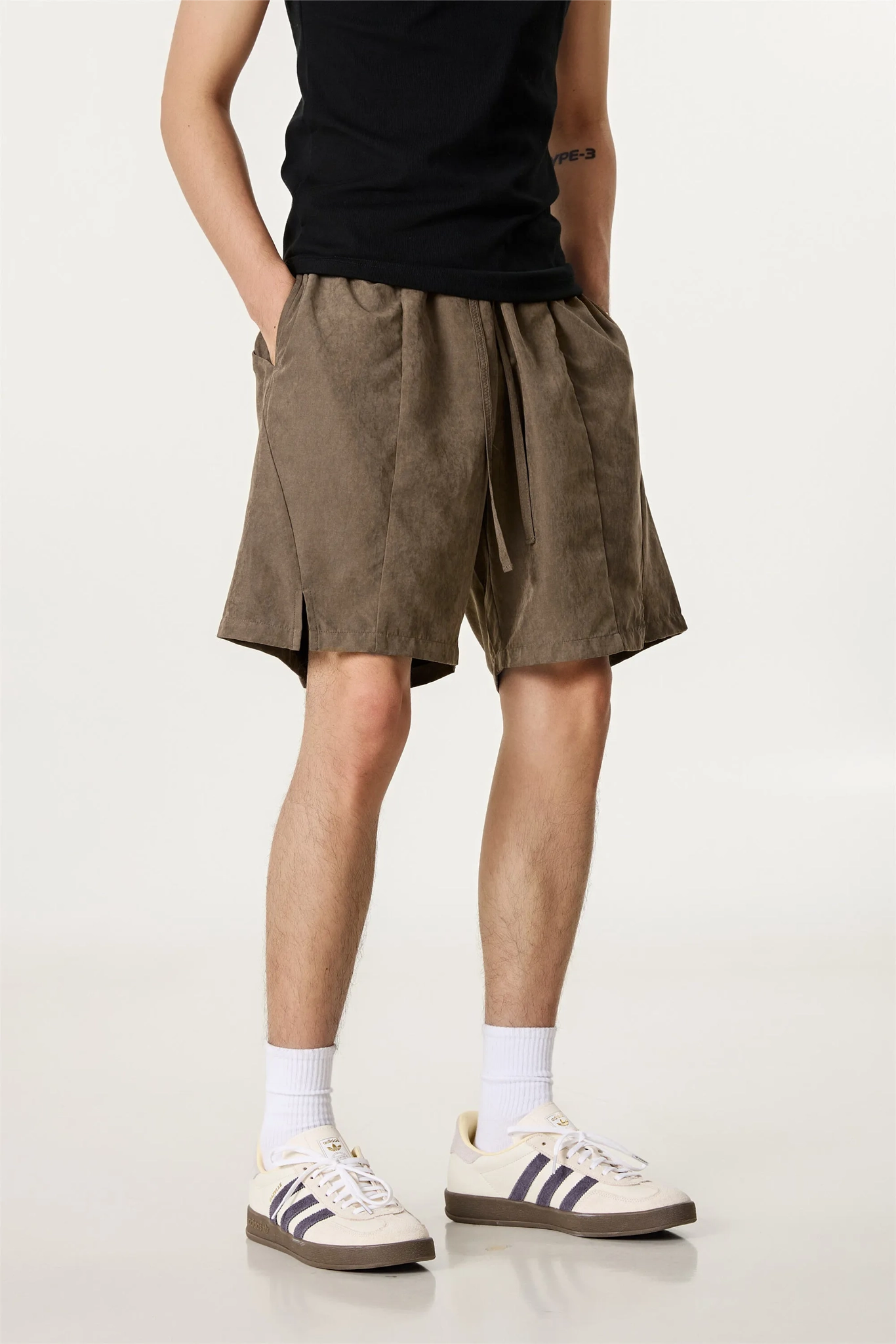 Person wearing brown shorts, black shirt, white socks, and Adidas shoes on a white background