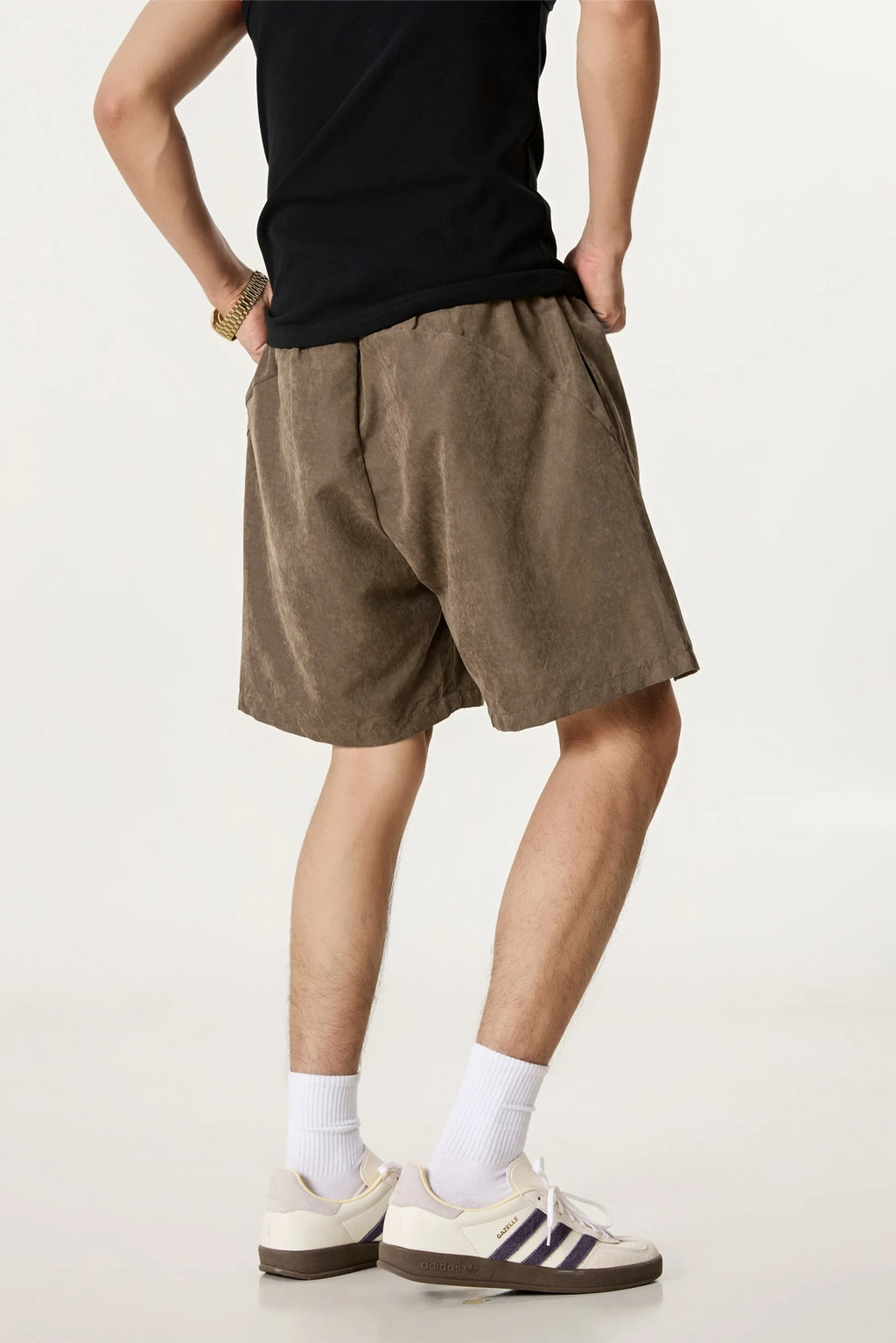 Person wearing brown shorts, black shirt, white socks, and sneakers on a plain background