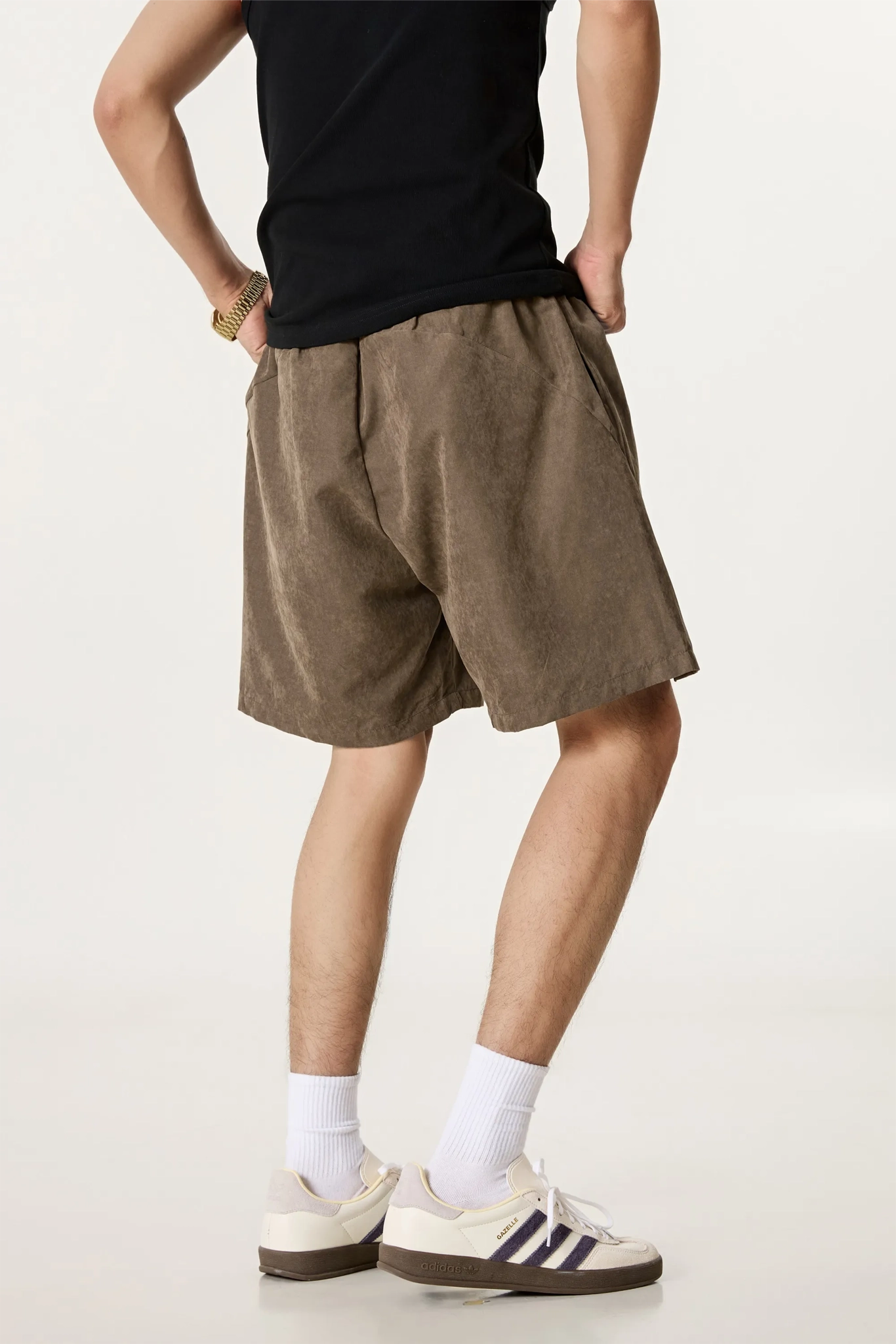 Person wearing brown shorts, black shirt, white socks, and sneakers on a plain background