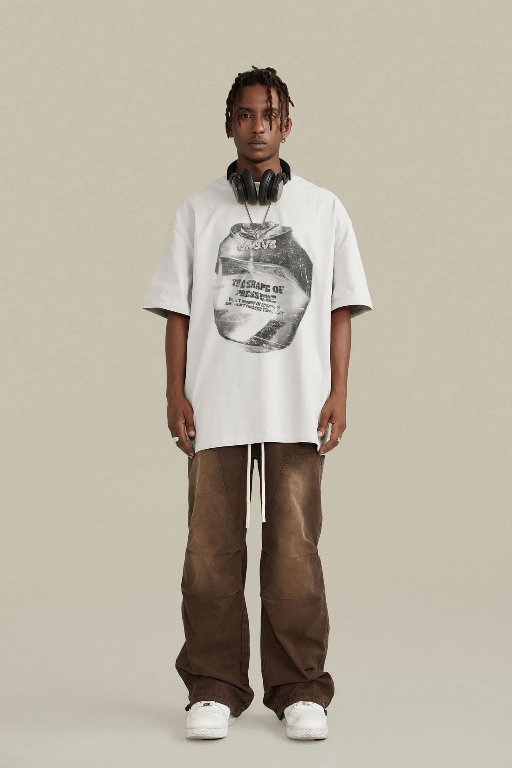 Person wearing a white t-shirt with graphic design and brown pants on a beige background