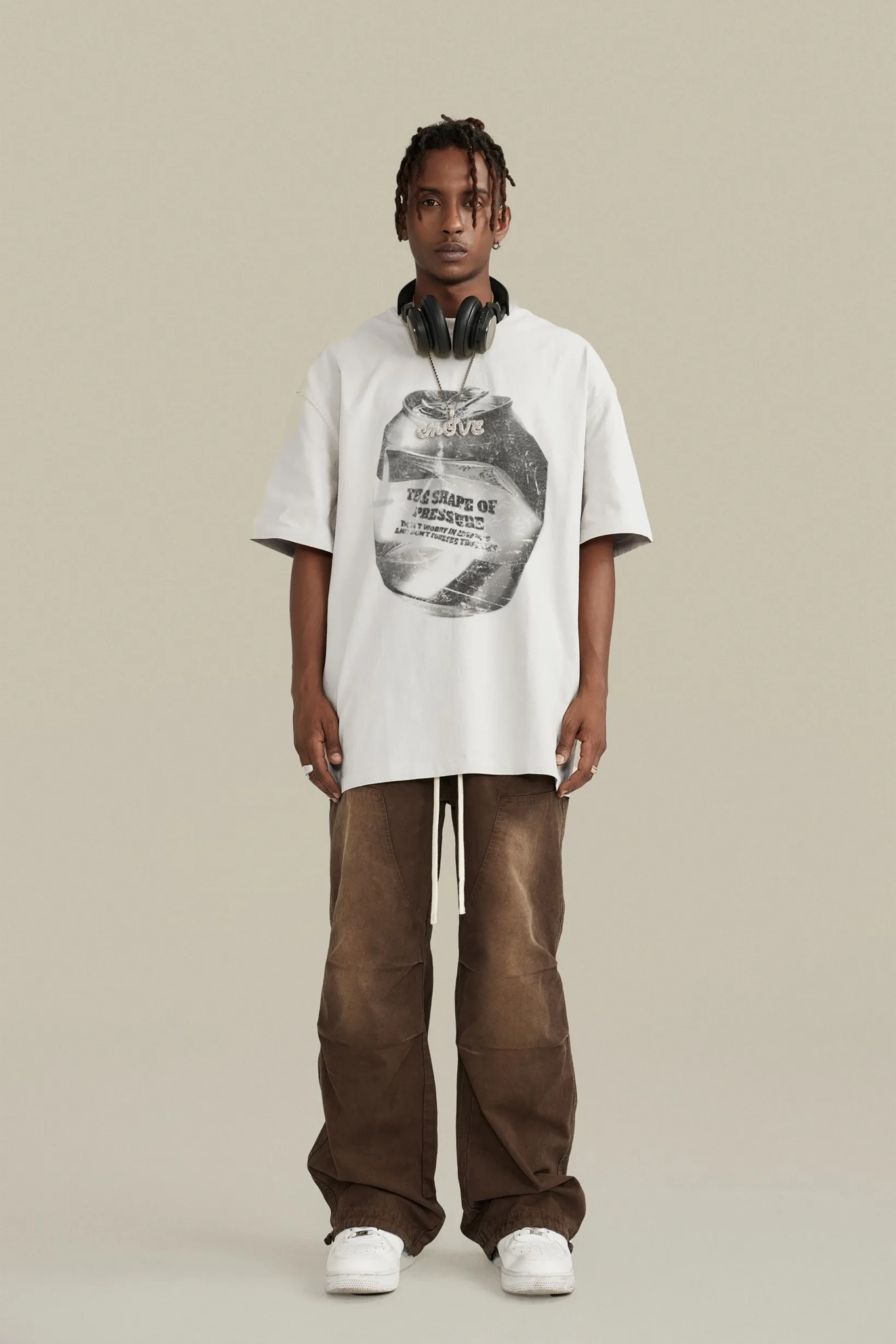 Person wearing a white t-shirt with graphic design and brown pants on a beige background