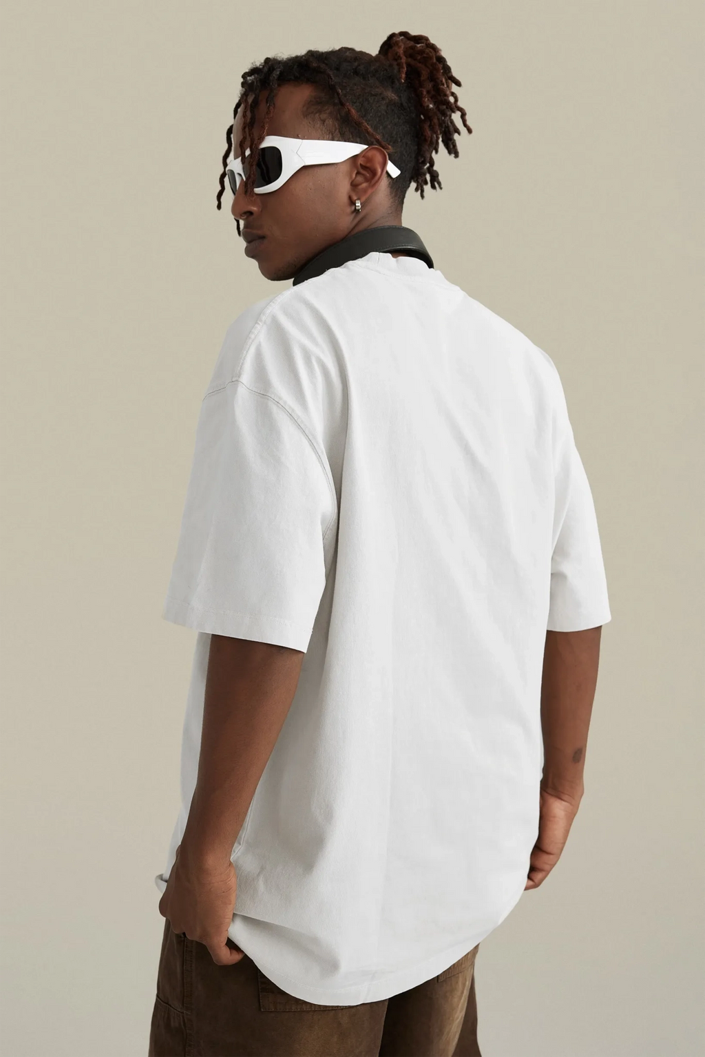 Person wearing a white oversized t-shirt and sunglasses on a beige background