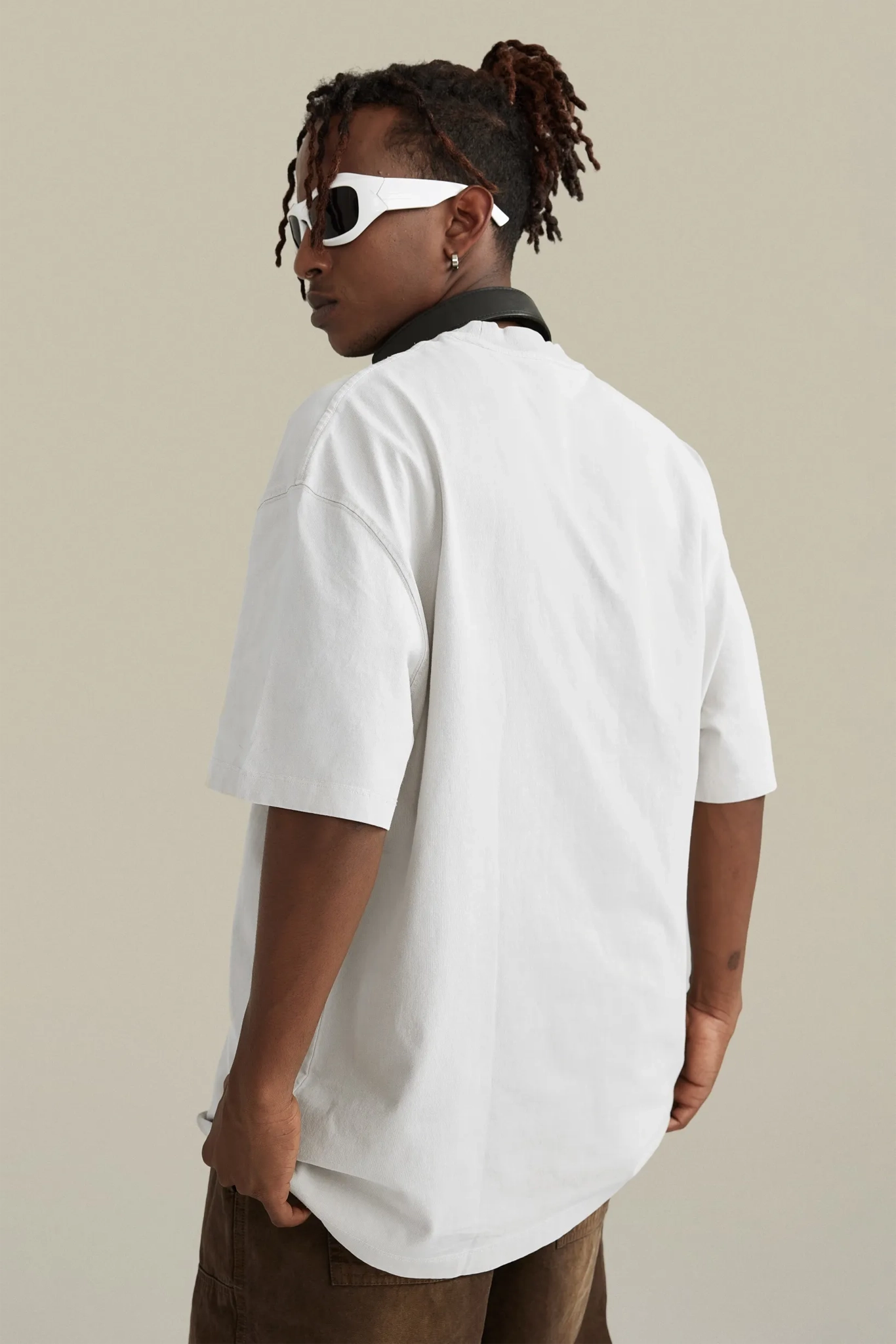 Person wearing a white oversized t-shirt and sunglasses on a beige background
