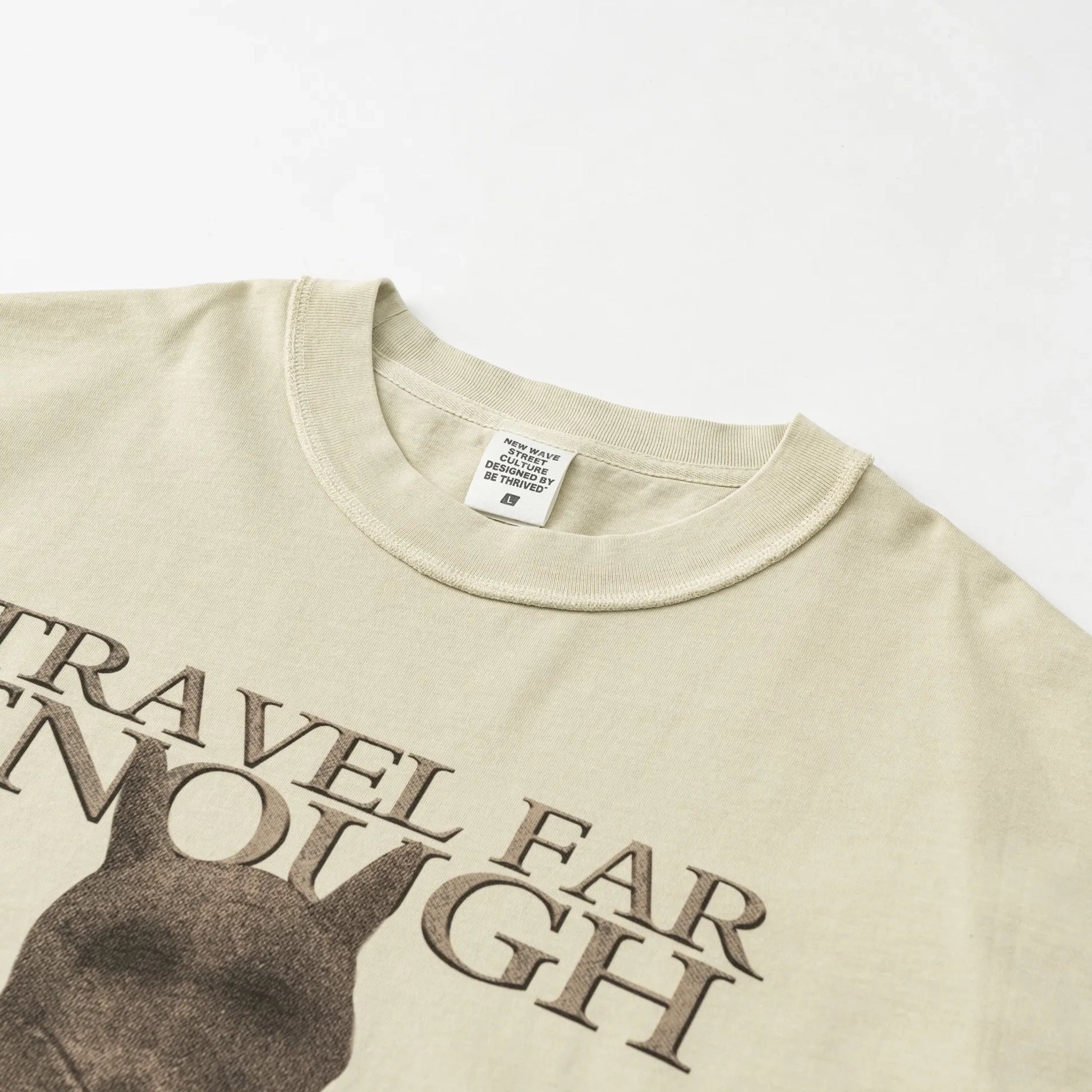 Beige t-shirt with text 'TRAVEL FAR ENOUGH' and a silhouette design on a white background.