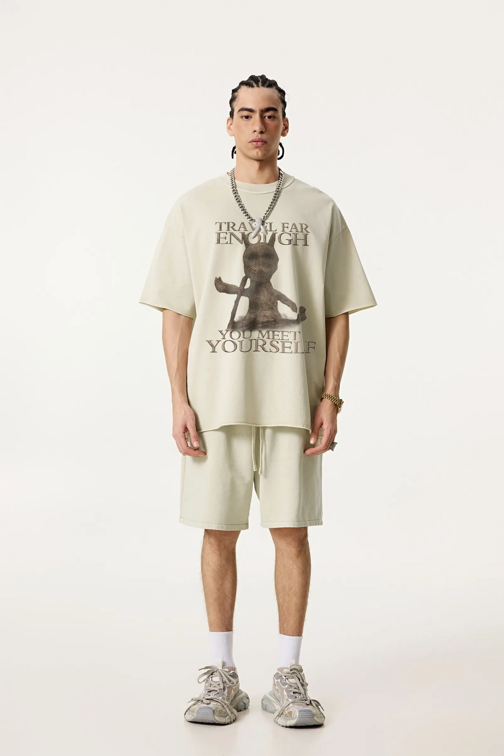 Person wearing a beige oversized t-shirt with a graphic design and text, standing against a white background.