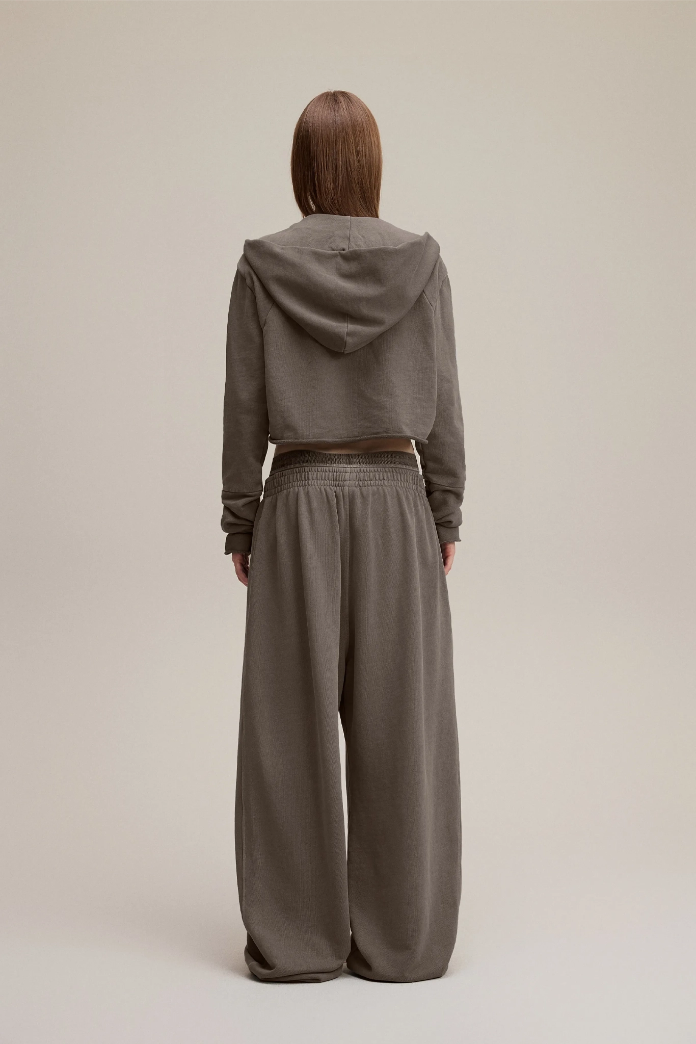 Person wearing a brown hoodie and wide-leg pants on a beige background