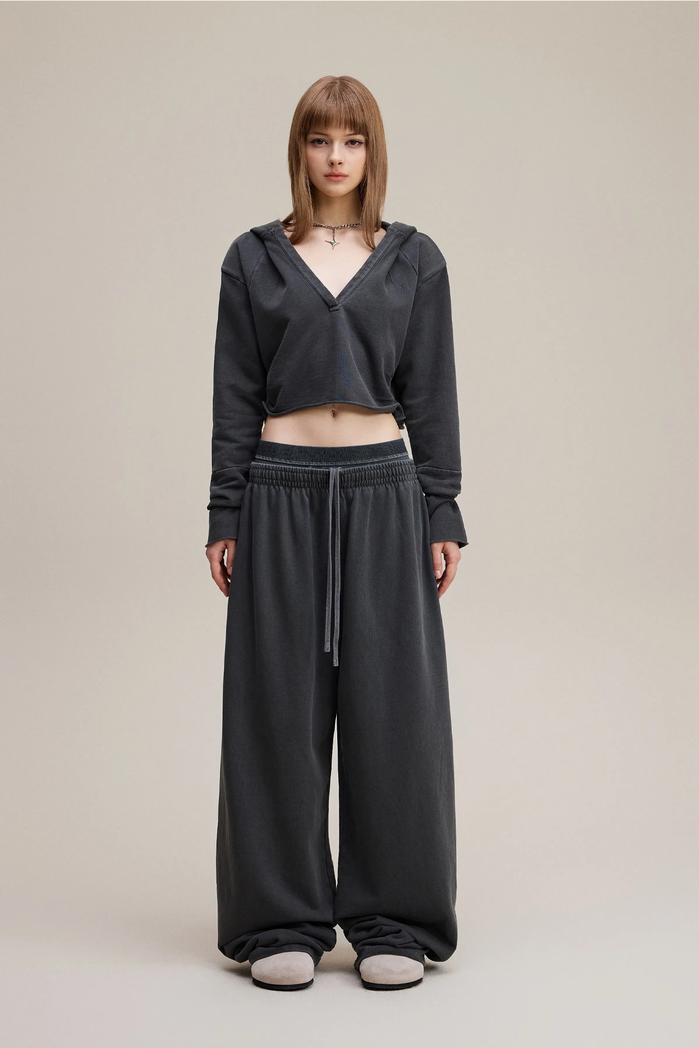 Person wearing a dark gray hoodie and wide-leg pants on a beige background