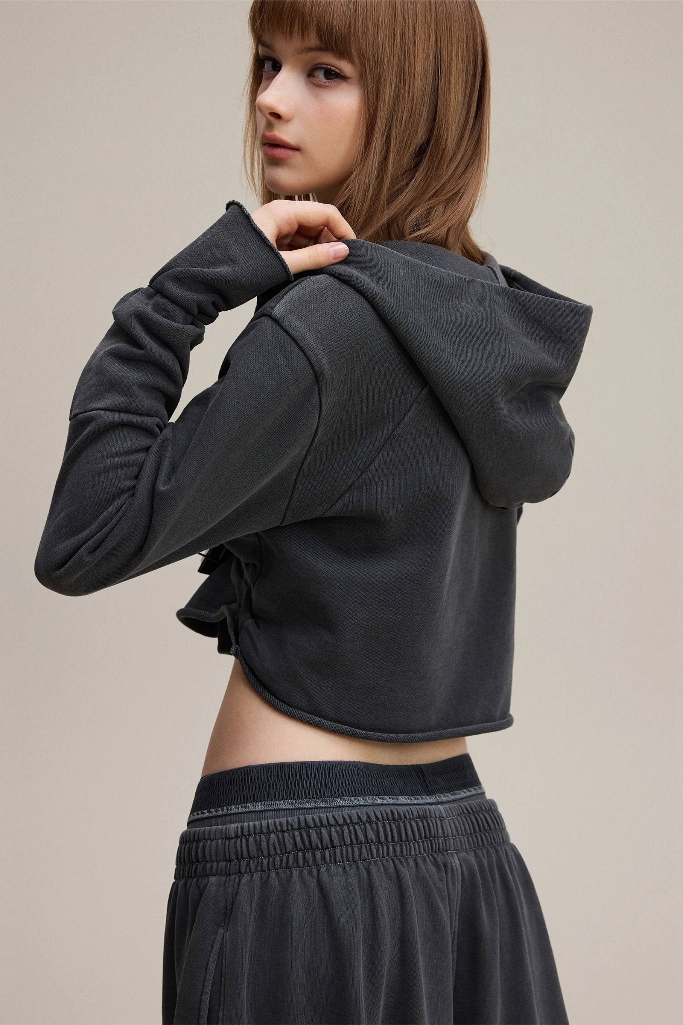 Person wearing a black cropped hoodie and pants on a beige background