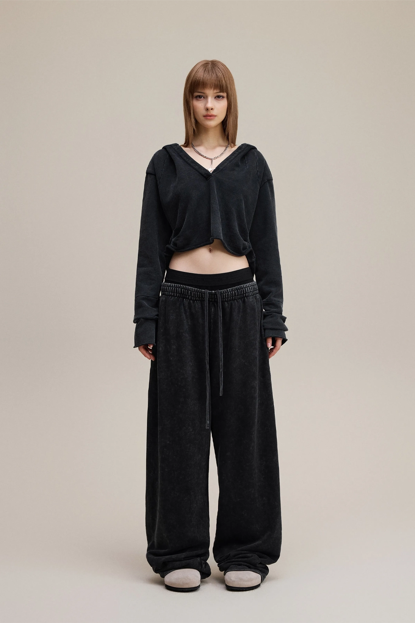 Person wearing a black hoodie and black pants on a beige background