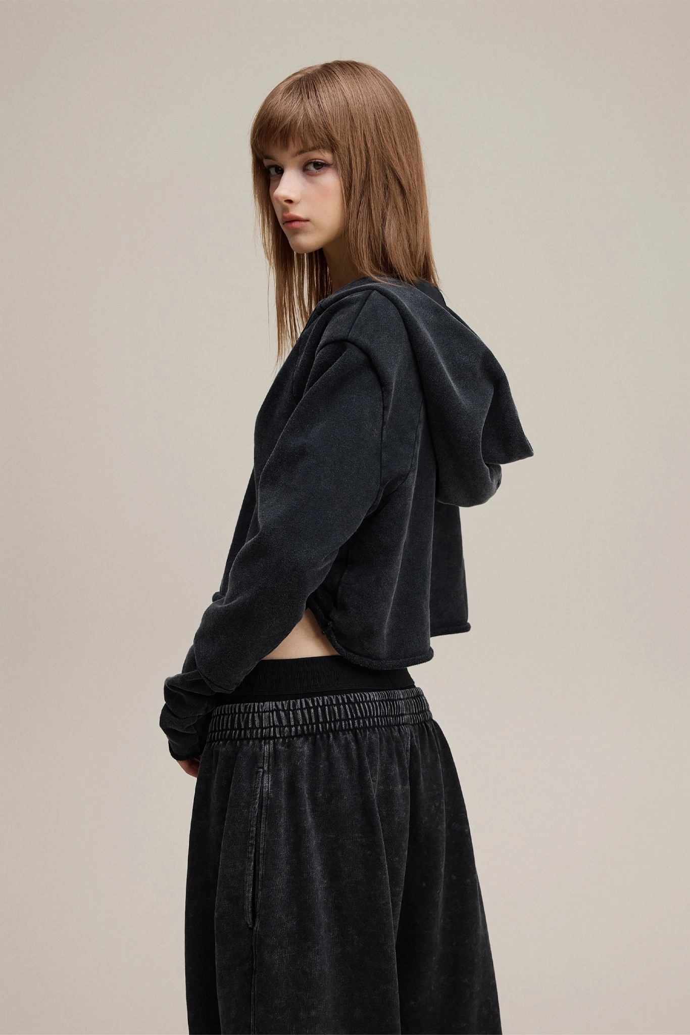 Person wearing a black hoodie and pants on a beige background