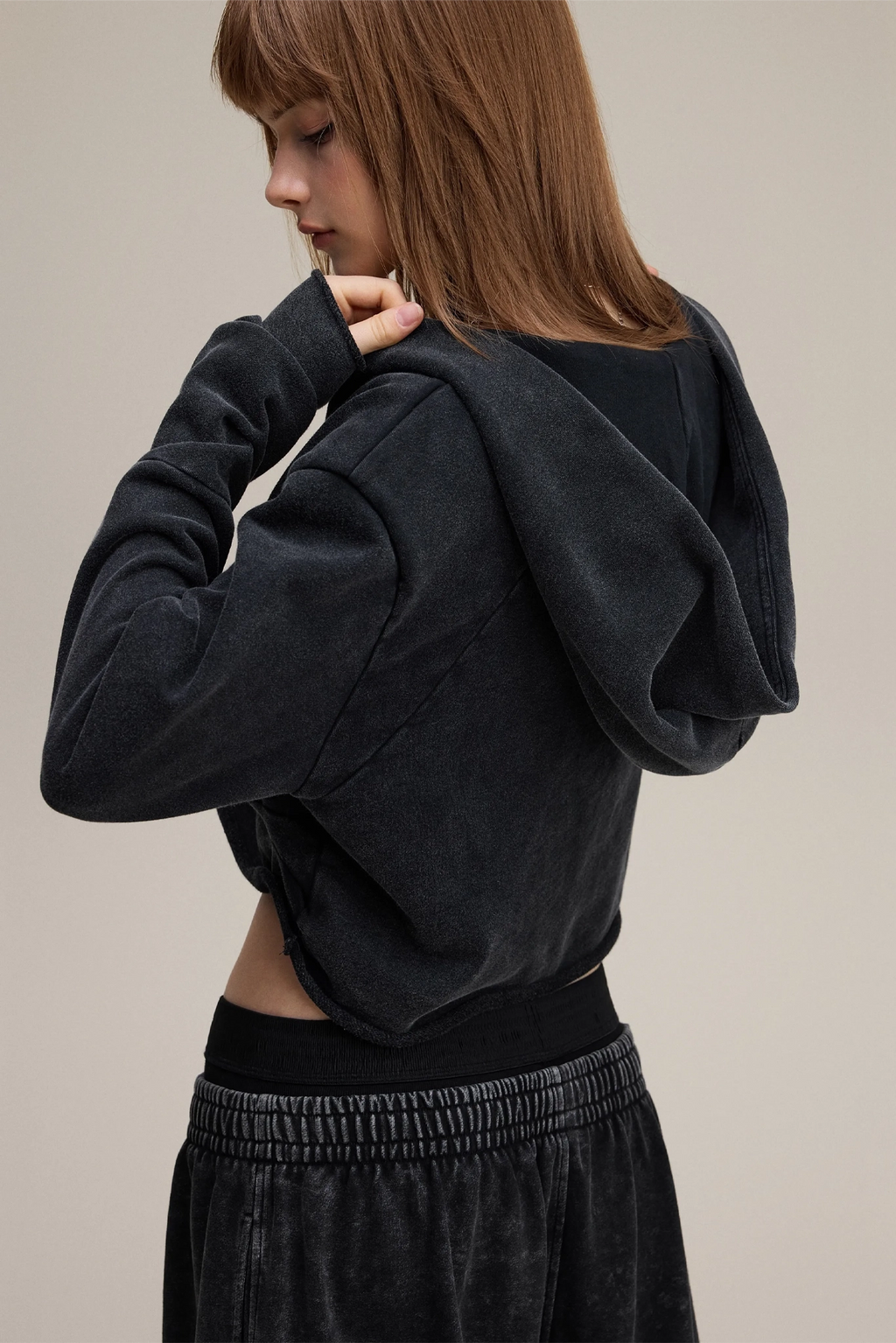 Person wearing a black hoodie and pants on a beige background