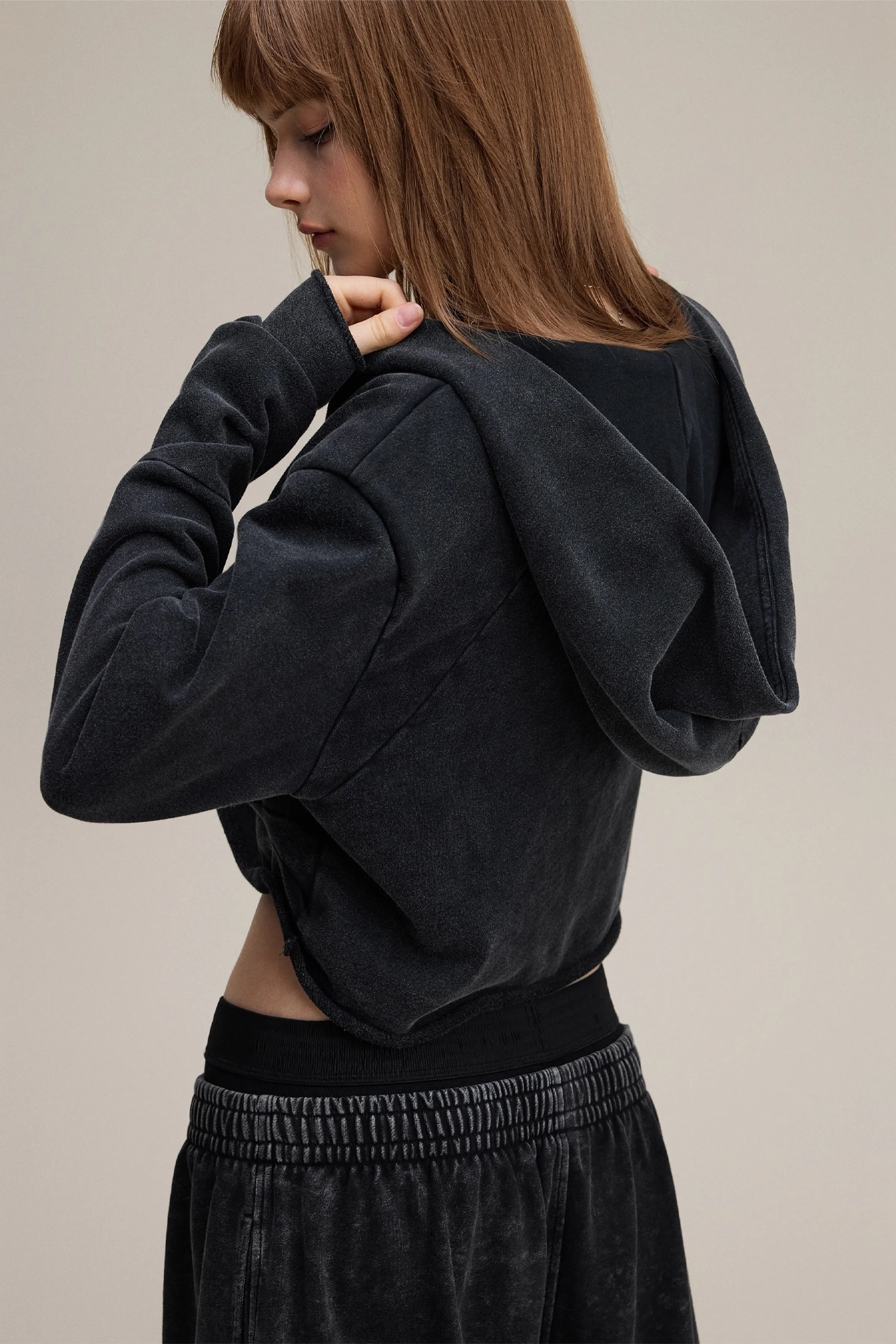 Person wearing a black hoodie and pants on a beige background