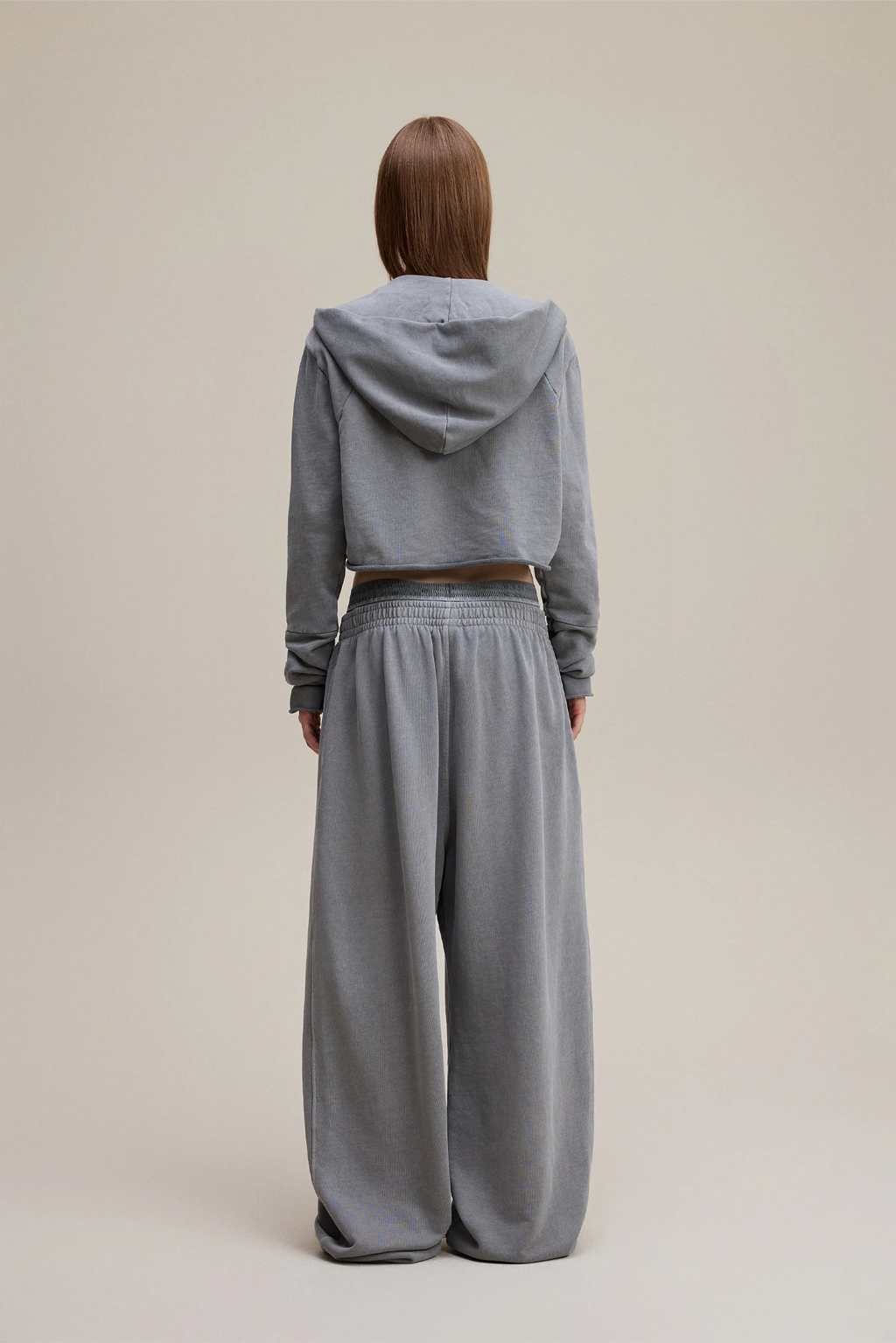 Person wearing a gray hoodie and pants on a beige background