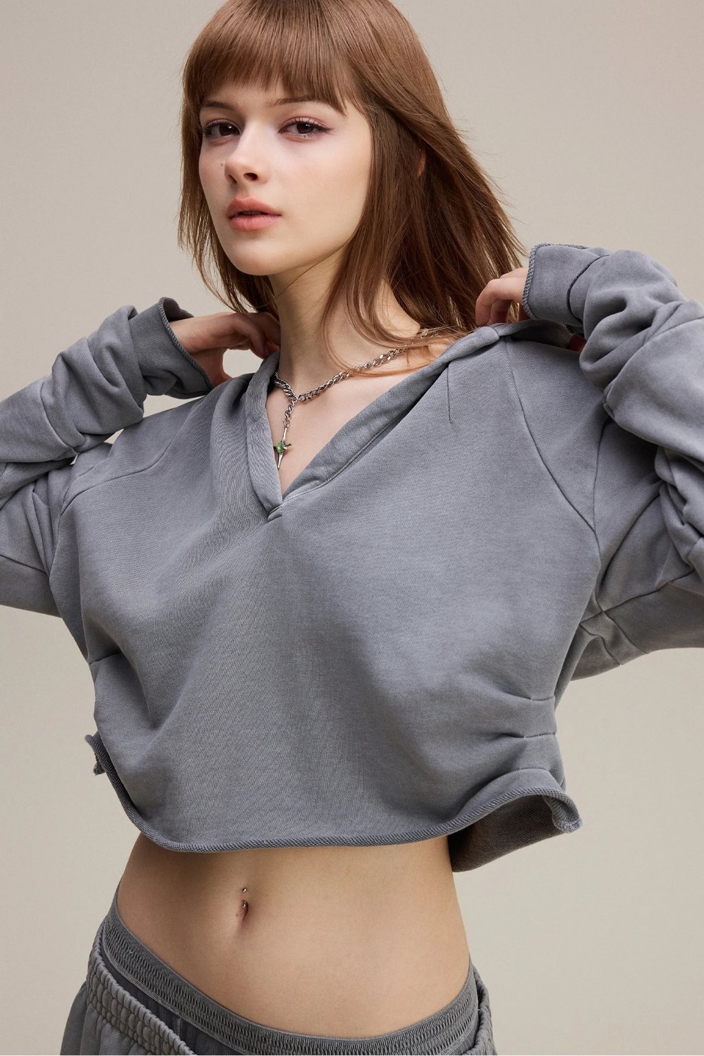 Woman wearing a gray cropped hoodie against a neutral background