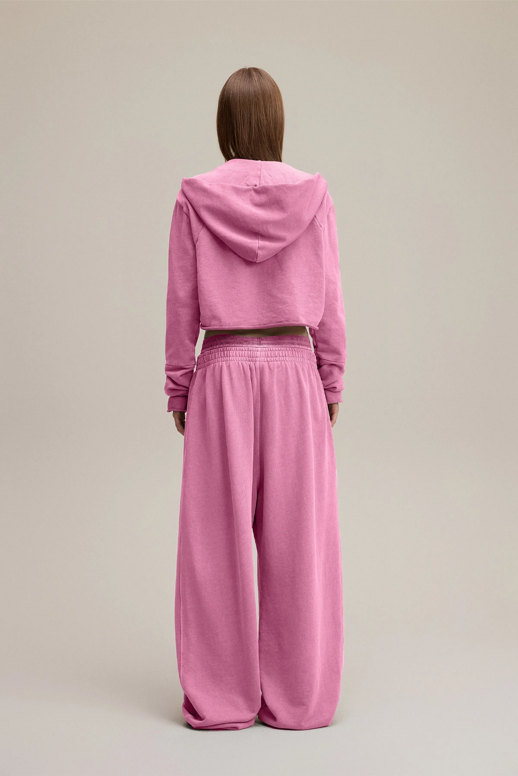Person wearing a pink hoodie and pants on a beige background