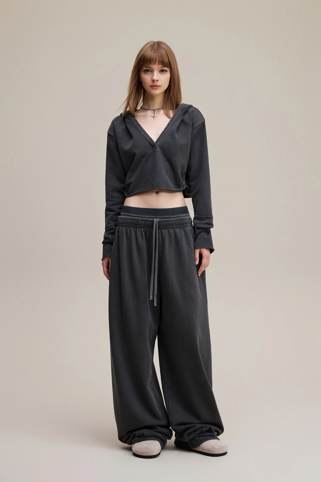 Woman wearing a dark gray outfit with a matching top and wide-leg pants on a beige background