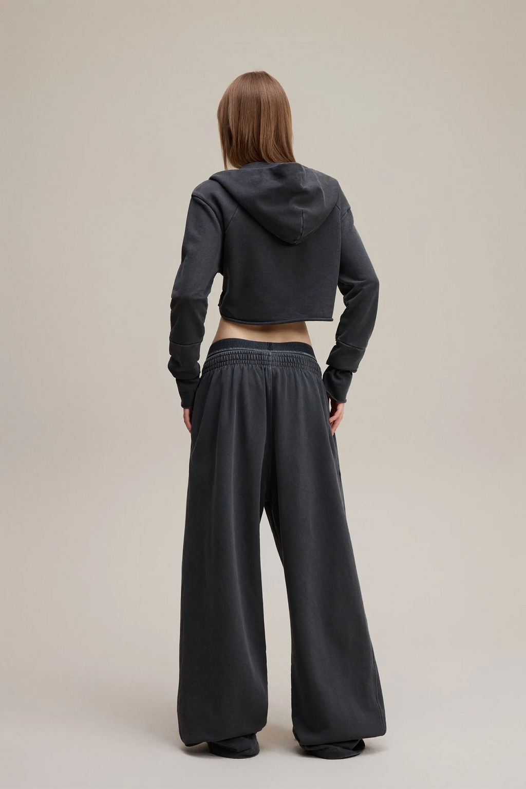 Person wearing a black hoodie and wide-leg pants on a beige background