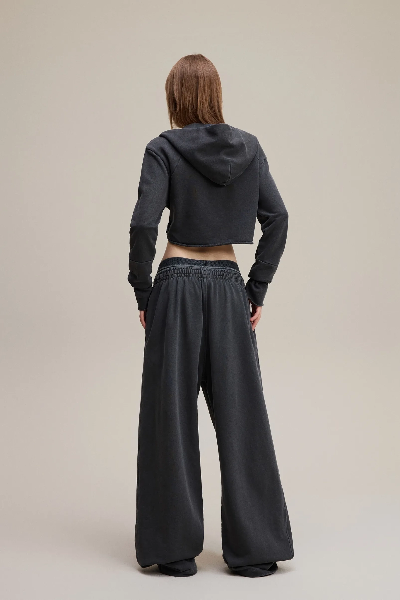 Person wearing a black hoodie and wide-leg pants on a beige background