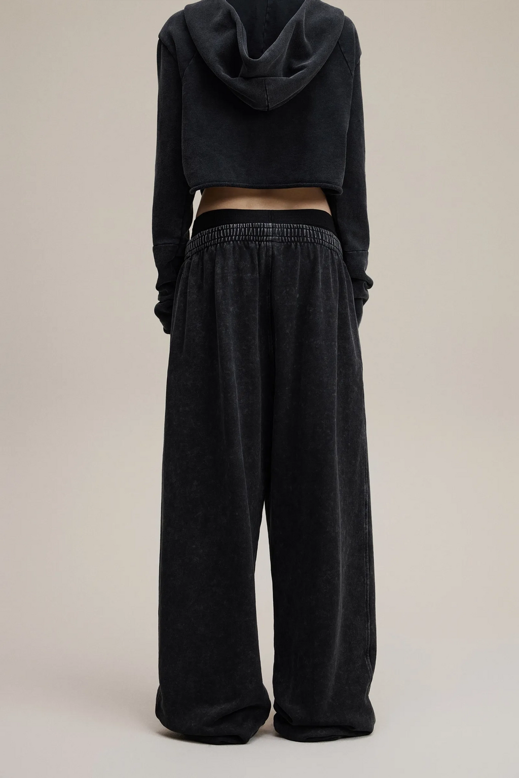Person wearing a black hoodie and wide-leg pants on a beige background