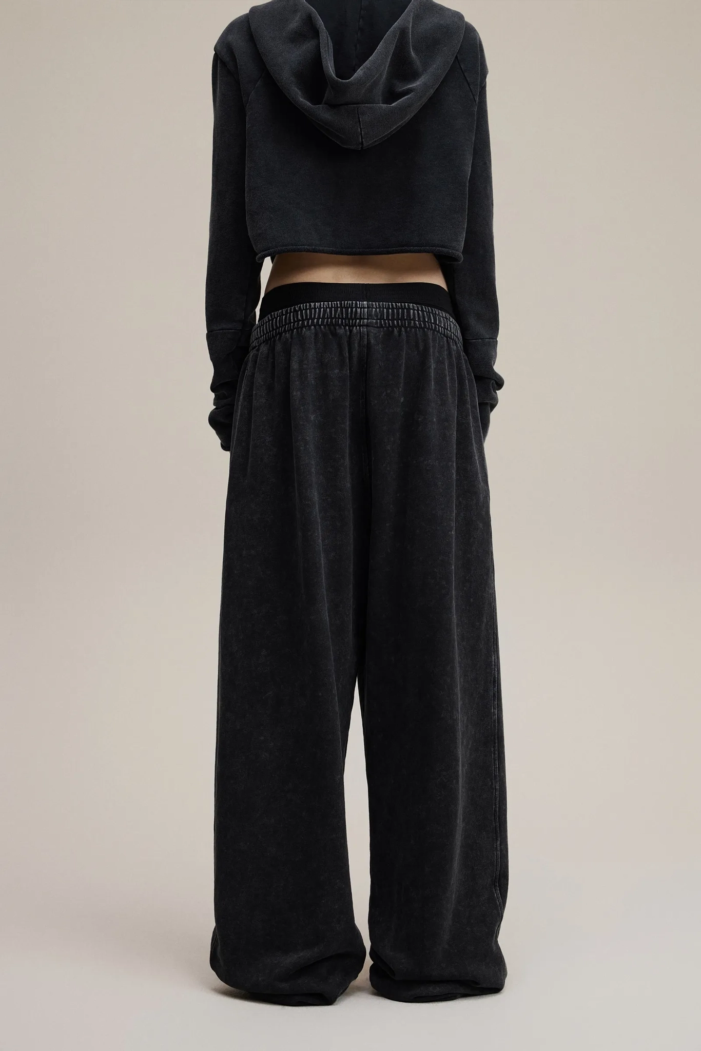 Person wearing a black hoodie and wide-leg pants on a beige background