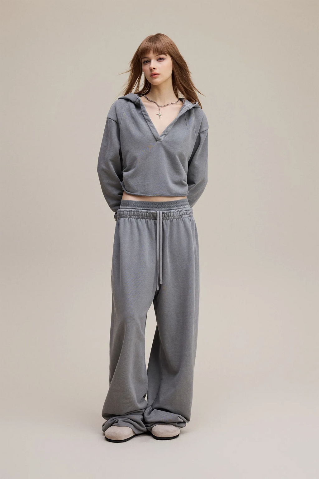 Person wearing a gray hoodie and pants on a beige background