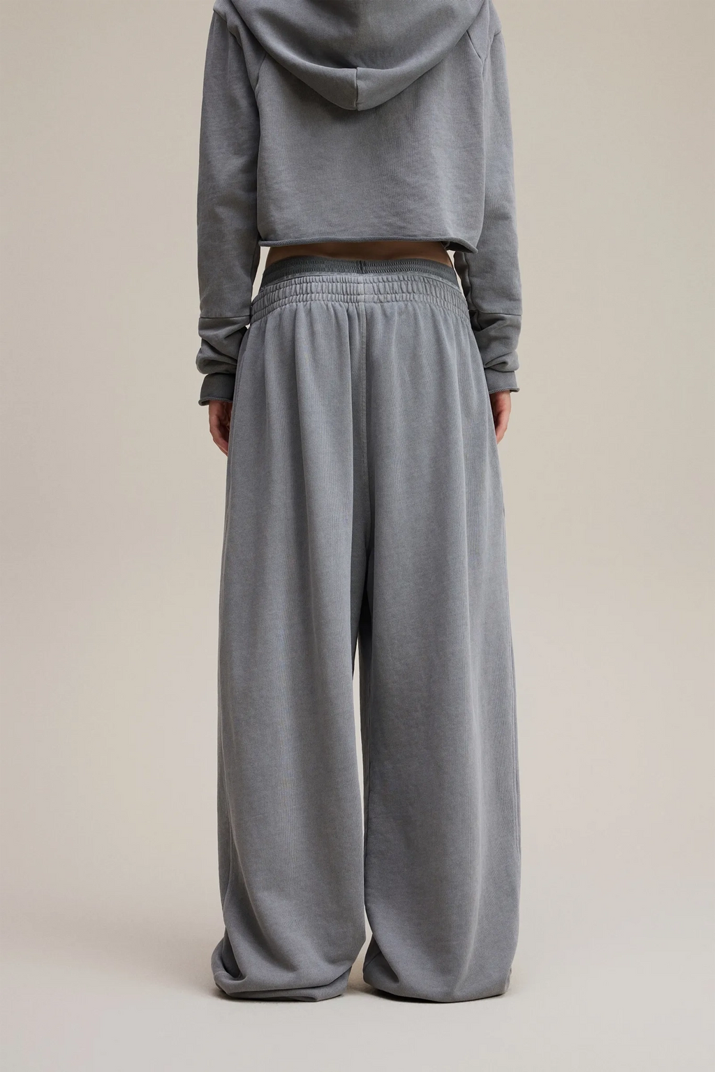 Person wearing a gray hoodie and wide-leg pants on a beige background