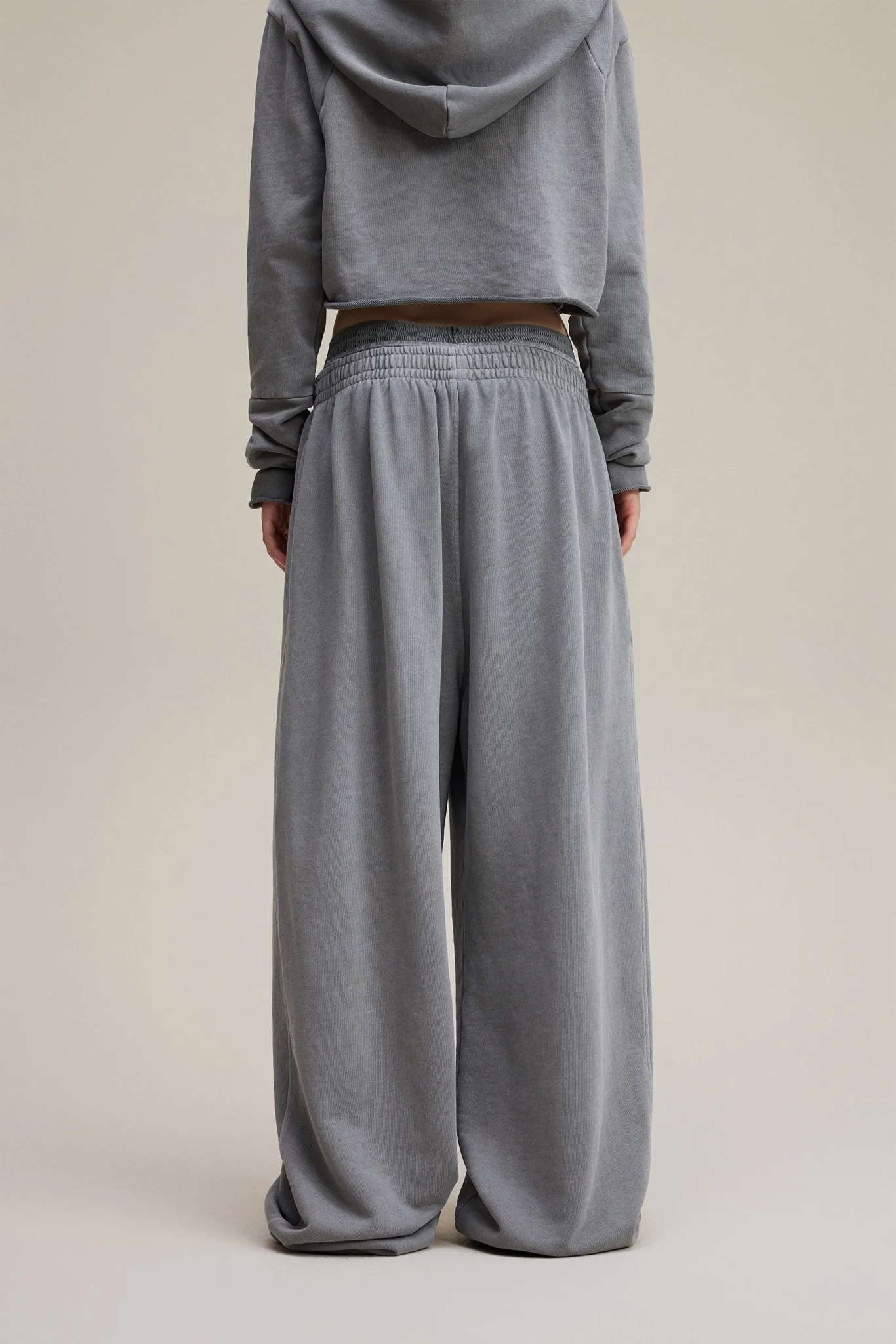 Person wearing a gray hoodie and wide-leg pants on a beige background