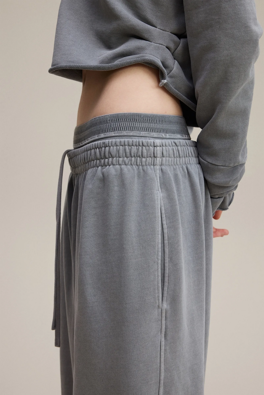 Person wearing gray sweatpants and a matching sweatshirt on a beige background